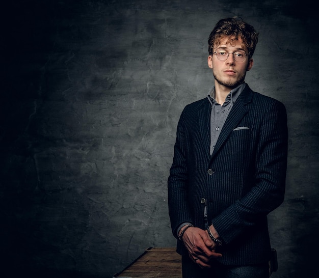 Portrait of a young handsome male with curly hair dressed in a jacket and eyeglasses.