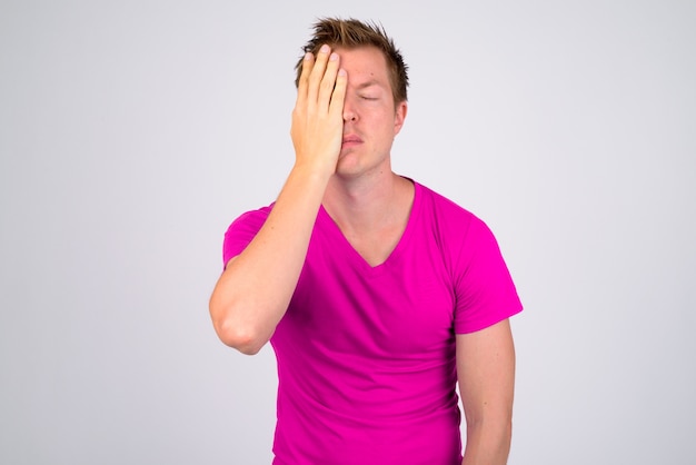 Portrait of young handsome man wearing purple shirt against white wall