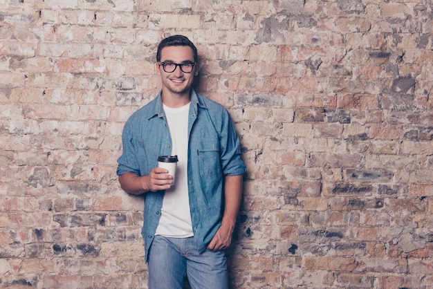 Portrait of young handsome man with cup of coffee on the space of brick wall