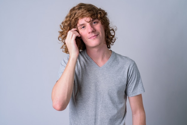 Portrait of young handsome man with long curly hair against white wall