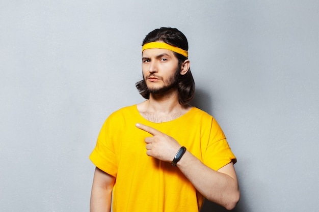 Portrait of young handsome man with long hair in yellow shirt, pointing finger away on