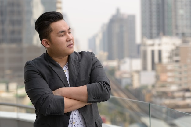 Portrait of young handsome overweight Filipino businessman in suit against view of the city