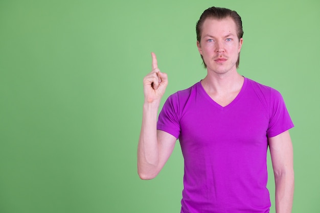 Portrait of young handsome Scandinavian man wearing purple shirt against chroma key or green wall