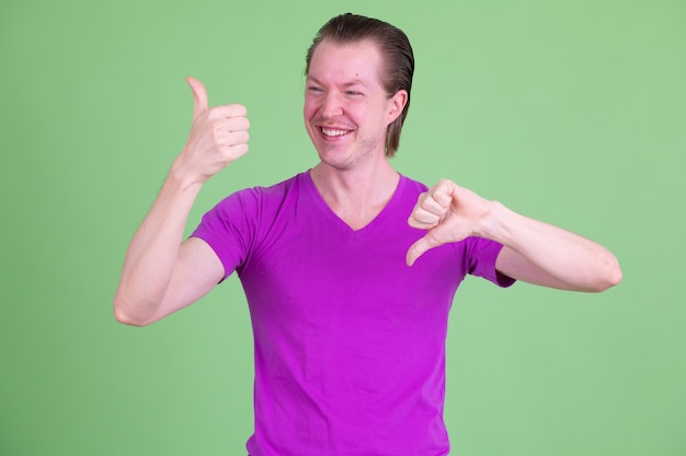 Portrait of young handsome Scandinavian man wearing purple shirt against chroma key or green wall