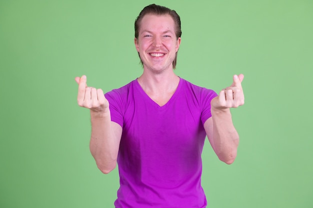 Portrait of young handsome Scandinavian man wearing purple shirt against chroma key or green wall