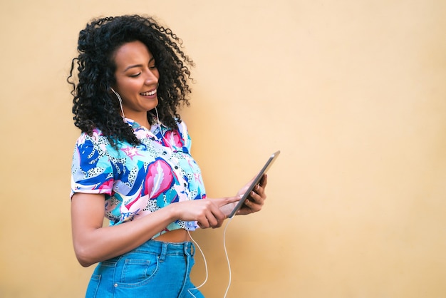 Portrait of young happy afro american latin woman listening music on her digital tablet. Technology concept.