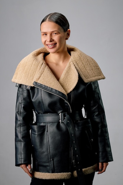 Photo portrait of a young happy brunette woman with braces on her teeth dressed in a sheepskin coat