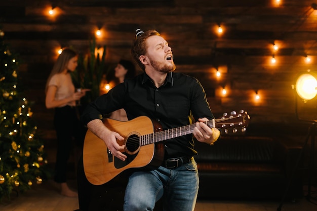 Portrait of young happy man in the festive hat singing with guitar