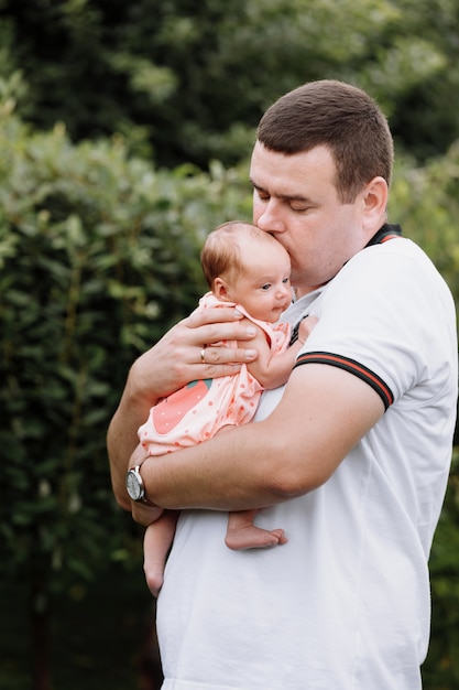 Portrait of young happy man holding his newborn cute babe dressed in white clothing.