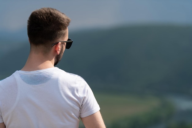 Portrait of a Young and Happy Man Standing at the Top of the Mountain Back to the Camera