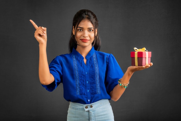 Portrait of young happy smiling Girl holding gift box on a grey background