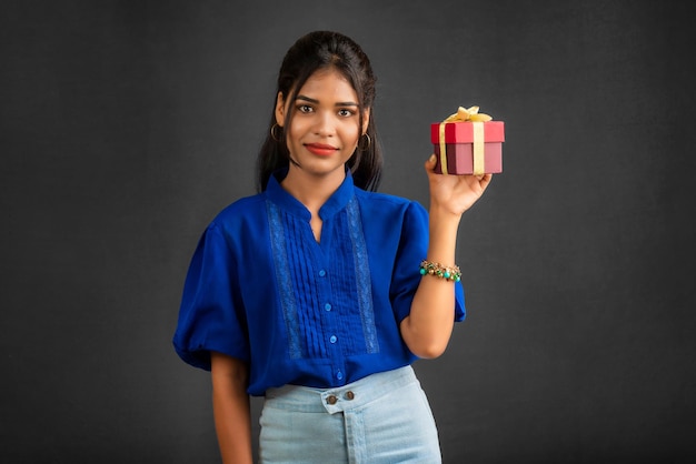 Portrait of young happy smiling Girl holding gift box on a grey background