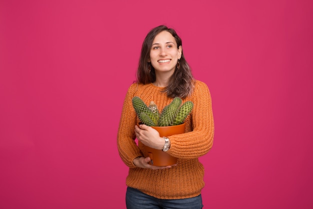 Portrait of young happy woman holding a big cactus plant while standing over pinky space