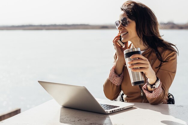 Portrait young happy woman talking on mobile phone working on laptop outside