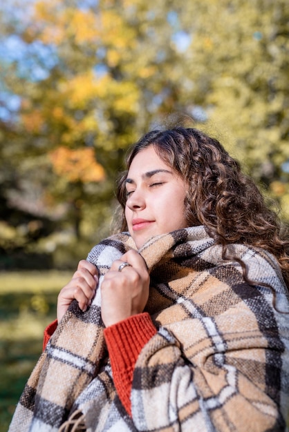 Portrait of young happy woman in warm plaid in autumn forest