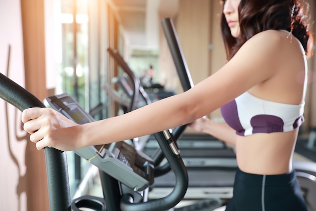 Portrait of young healthy and sporty woman using exercise machine in gym 