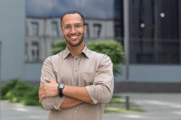 Portrait of young hispanic student man smiling and looking at camera near university campus with