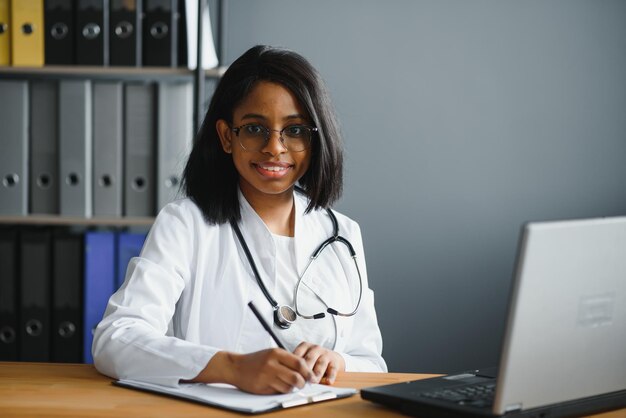 Portrait of young indian doctor working in the hospital while looking at laptop and write on clipboard