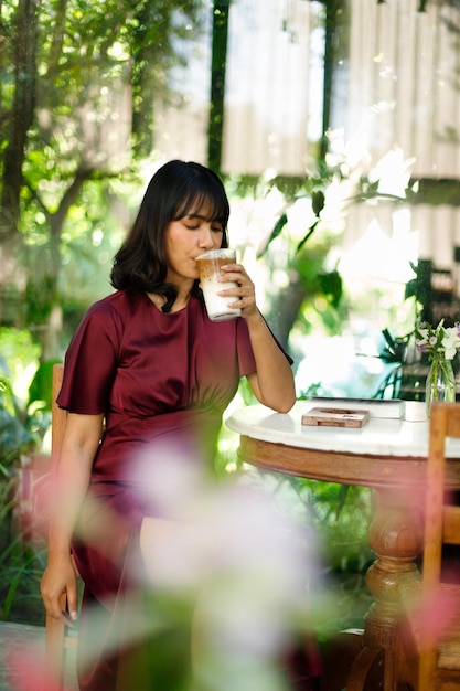 Portrait of young Indian female in coffee shop with relax environment, Tanned skin Asian woman purple dress feel smile happy in calm nature and ice coffee with morning sun through lace curtain