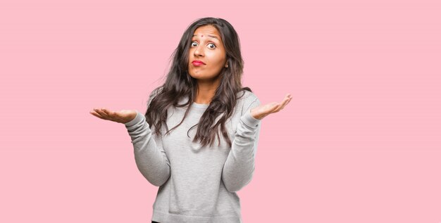 Portrait of young indian woman doubting and shrugging shoulders