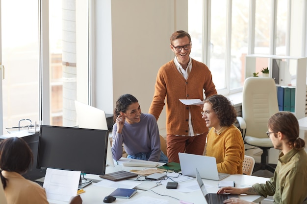 Portrait of young IT development team discussing project and smiling while enjoying work in software production office, copy space