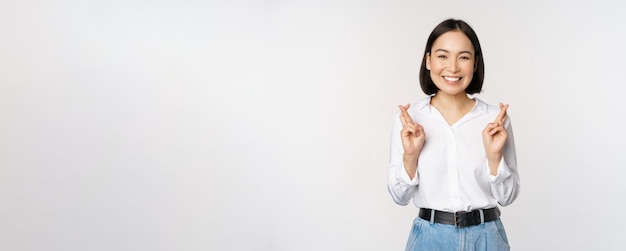 Portrait of young korean woman asian girl cross fingers and praying making wish anticipating waiting