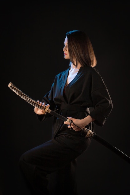 Portrait of young kung fu brunette girl with wakizashi on black background