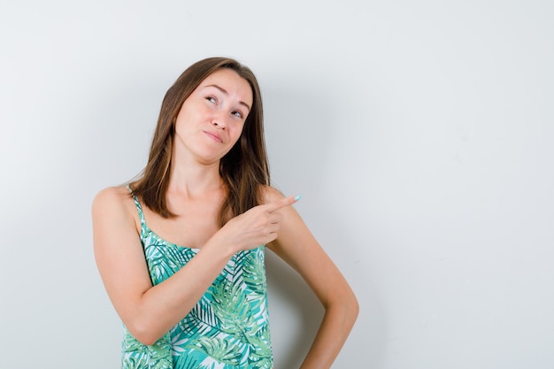 Portrait of young lady pointing to the right side in blouse and looking pensive front view