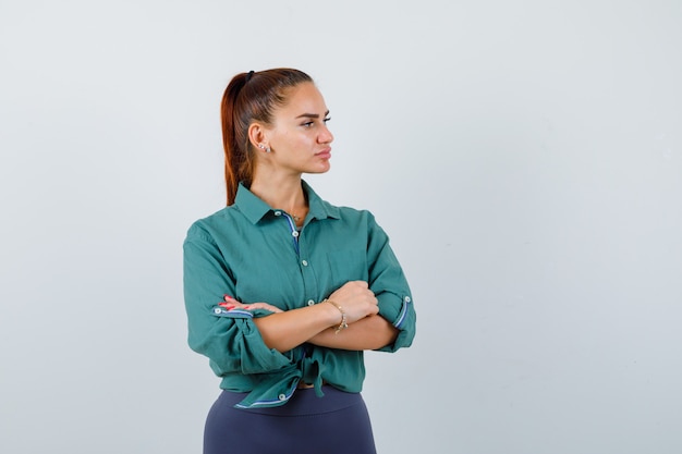 Portrait of young lady standing with crossed arms while looking away in green shirt and looking pensive front view