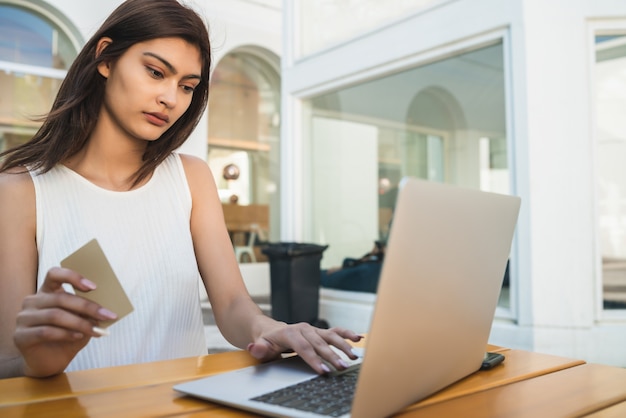 Portrait of young latin woman holding credit card and using laptop to shop online at a coffee shop. Shopping online and lifestyle concept.