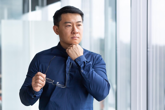 Portrait of a young male asian teacher he is standing in the office campus holding glasses