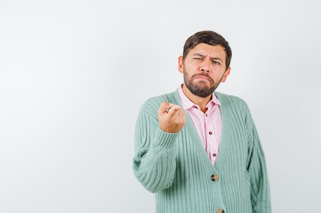 Portrait of young male pointing at front in shirt, cardigan and looking hesitant front view