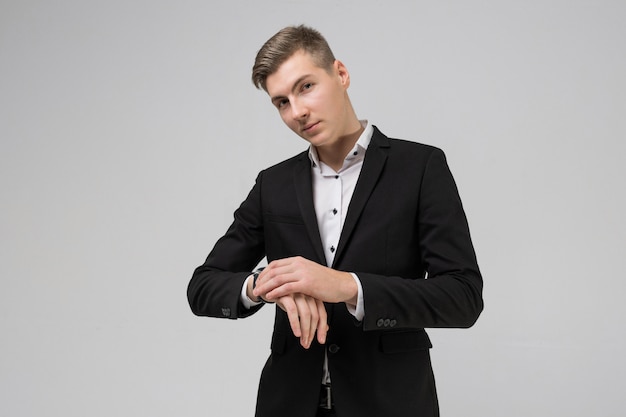 Portrait of a young man in a black suit straightening watch on white