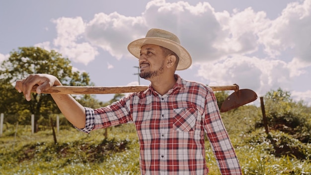 Portrait of young man in the casual shirt holding his hoe in the farm Farm tool Latin man