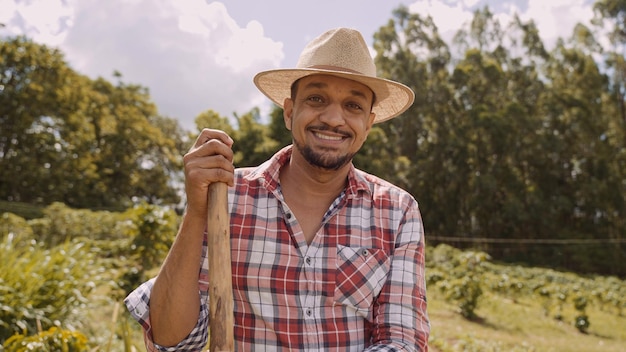 Portrait of young man in the casual shirt holding his hoe in the farm Farm tool Latin man