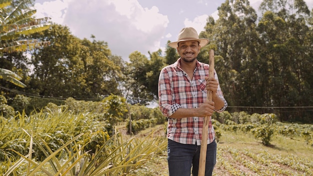 Portrait of young man in the casual shirt holding his hoe in the farm Farm tool Latin man