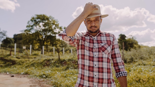 Portrait of young man in the casual shirt putting on the hat in the farm