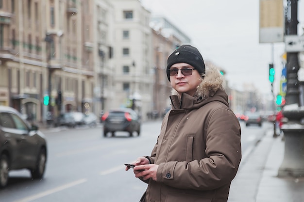 Portrait of young man in casual winter clothes with glasses on walk city