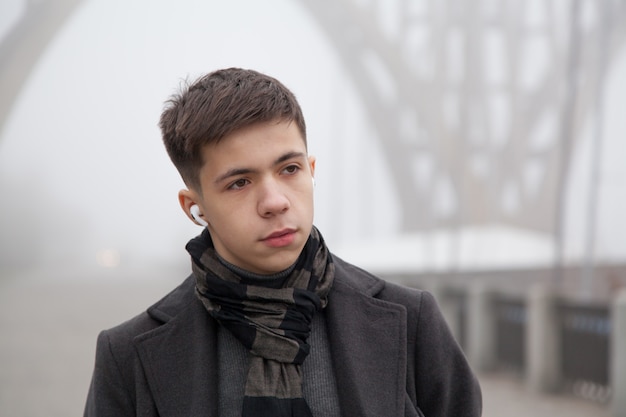 Portrait of a young man on a city promenade, foggy winter weather. Photo in gray tones