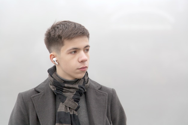 Portrait of a young man on a city promenade, foggy winter weather. Photo in gray tones