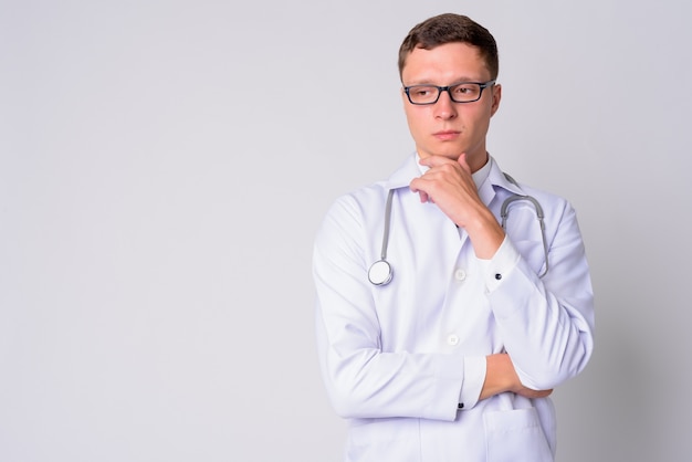 Portrait of young man doctor wearing eyeglasses against white wall