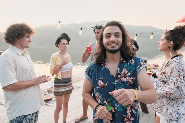 Portrait of young man drinking beer and smiling at camera while having fun at a party