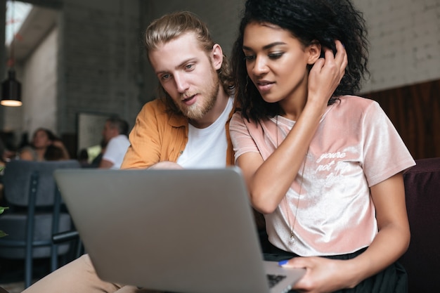 Portrait of young man and girl sitting at the restaurant and working on laptop