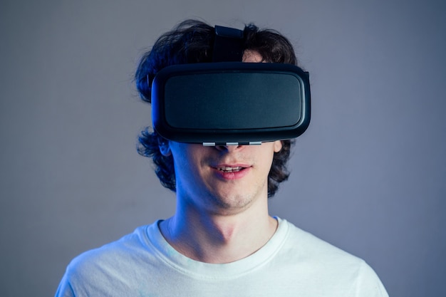 Portrait of a young man in the glasses of virtual reality on a gray wall background. The concept of games in the mask of virtual reality