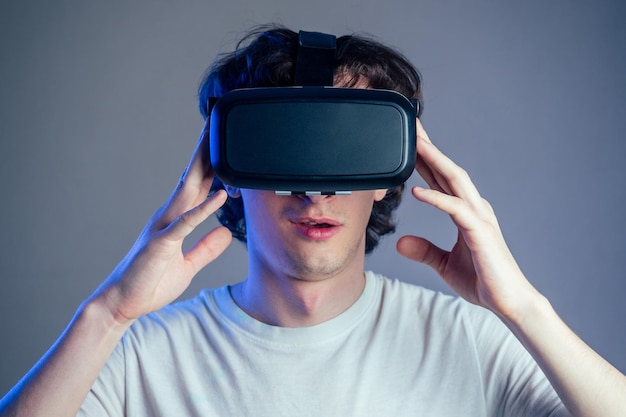 Portrait of a young man in the glasses of virtual reality on a gray wall background. The concept of games in the mask of virtual reality