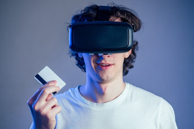 Portrait of a young man in glasses virtual reality holds a credit card. the concept of games in a mask of virtual reality, online shopping and buying