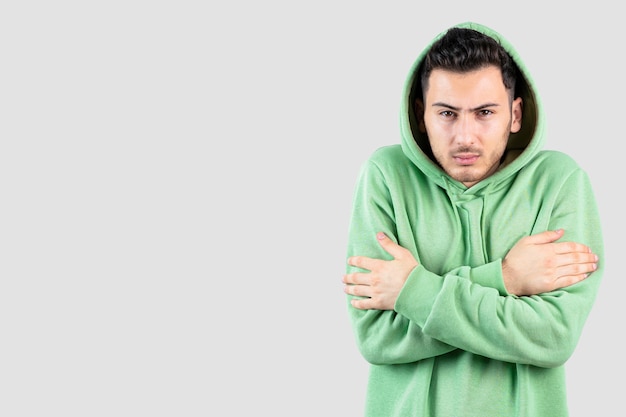 Portrait of young man in hoodie feeling cold over white