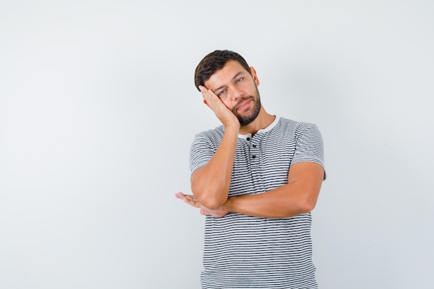 Portrait of young man leaning cheek on palm in t-shirt and looking pensive front view