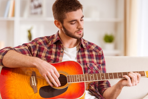 Portrait of a young man playing the guitar at home.