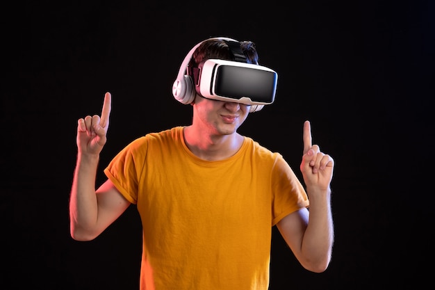 Portrait of young man playing vr in headphones on a dark wall